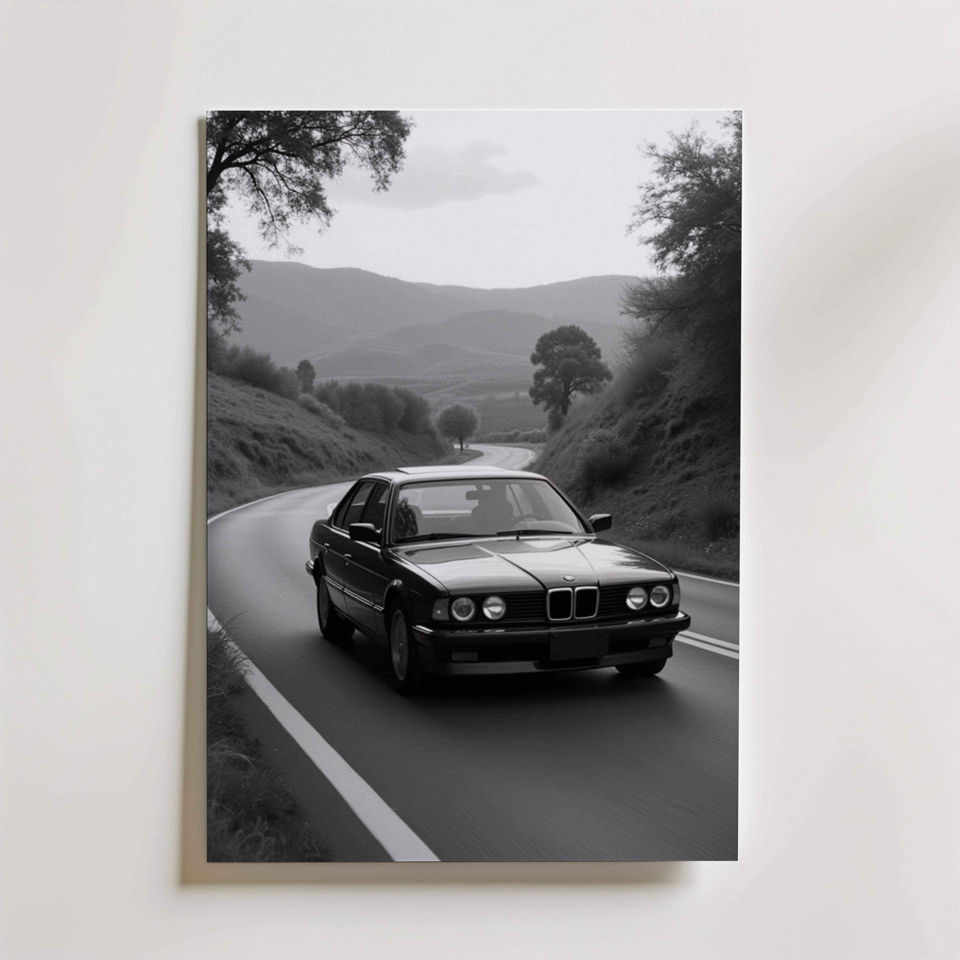 Vintage BMW Poster by Bozetto: Svartvitt foto av en klassisk sedan som kör på en slingrande väg genom kullar, omgiven av träd och berg, tryckt på premiumpapper med en lyxig matt finish.